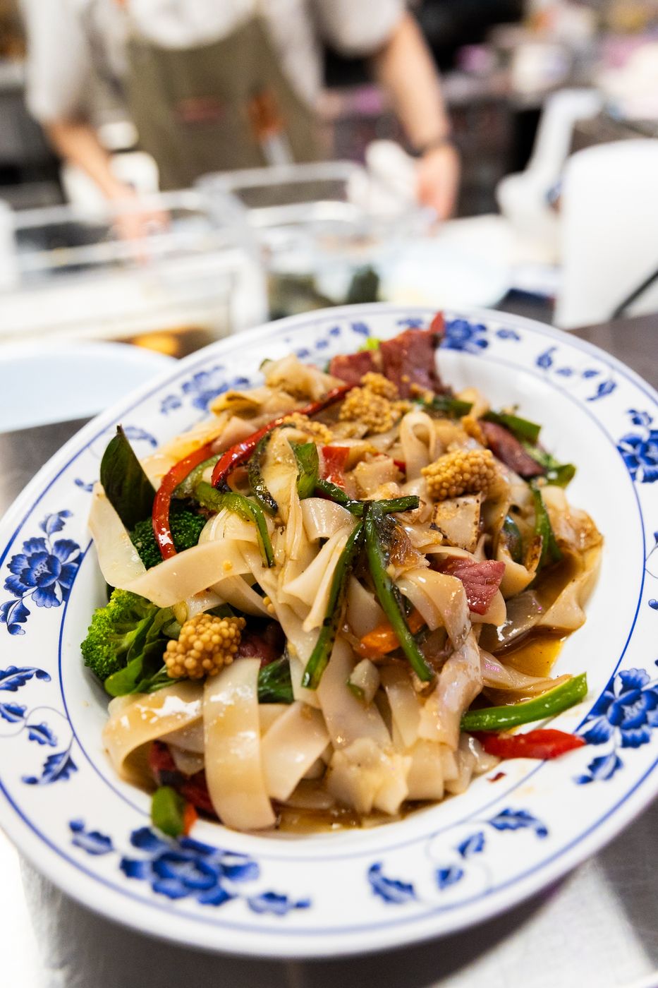Drunken noodles with pastrami, wide rice noodles and peppers on a blue and white plate