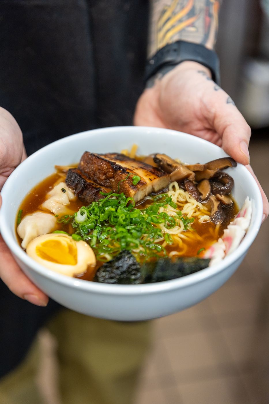 A bowl of pork ramen with ramen egg, nori and scallion, held out across the counter