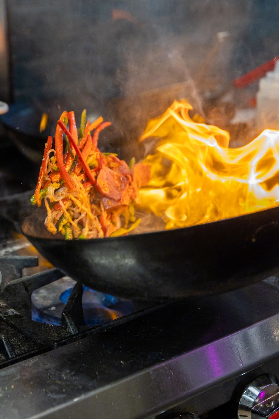 Drunken noodles hitting a wok over a high flame